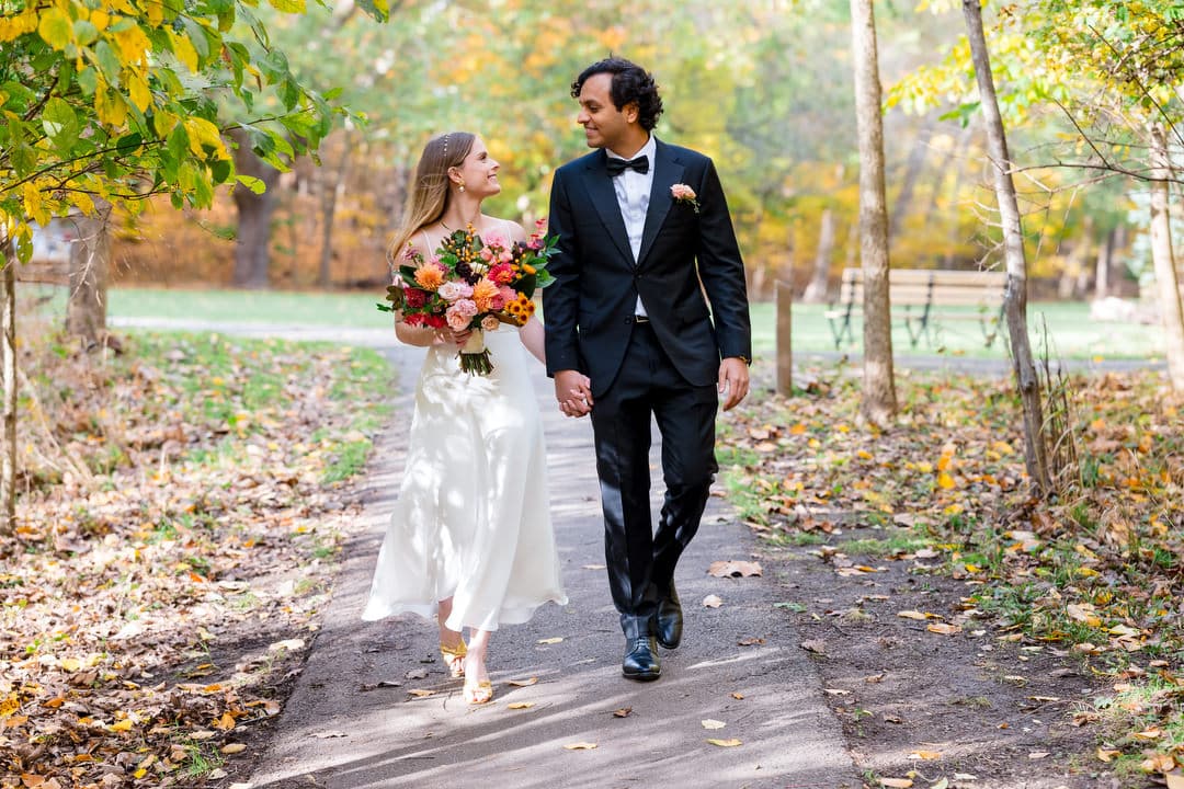 A bride wearing a white dress carries a colorful bouquet as she walks with her groom who is wearing a black tuxedo.