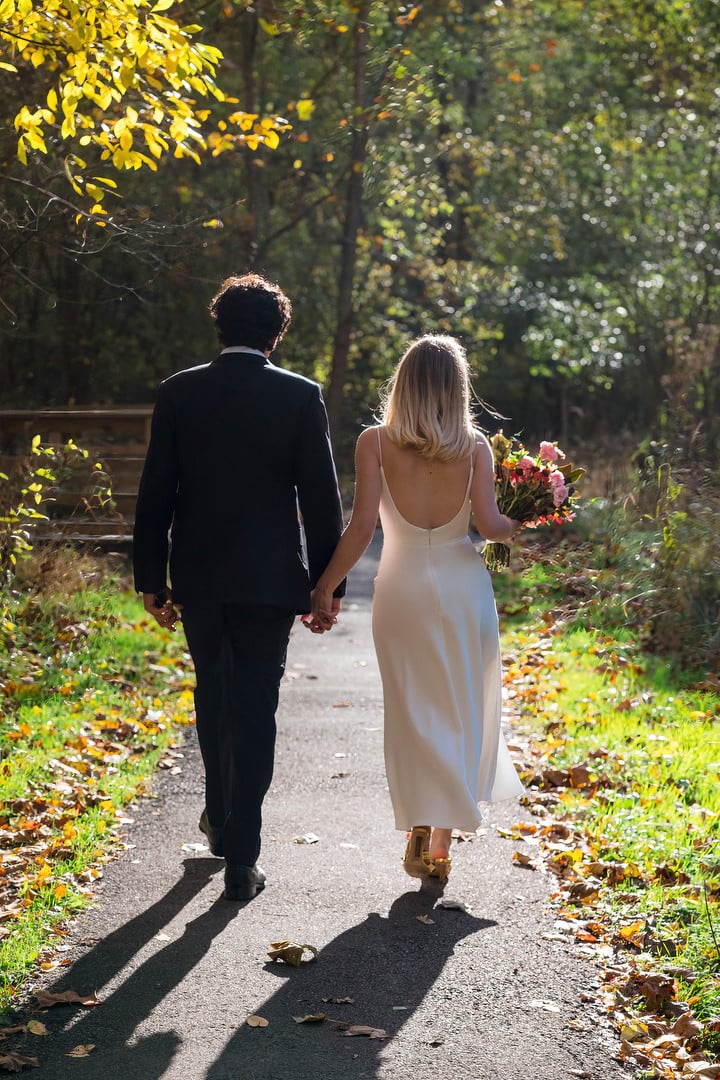 A bride and groom walk along a path away from the camera.
