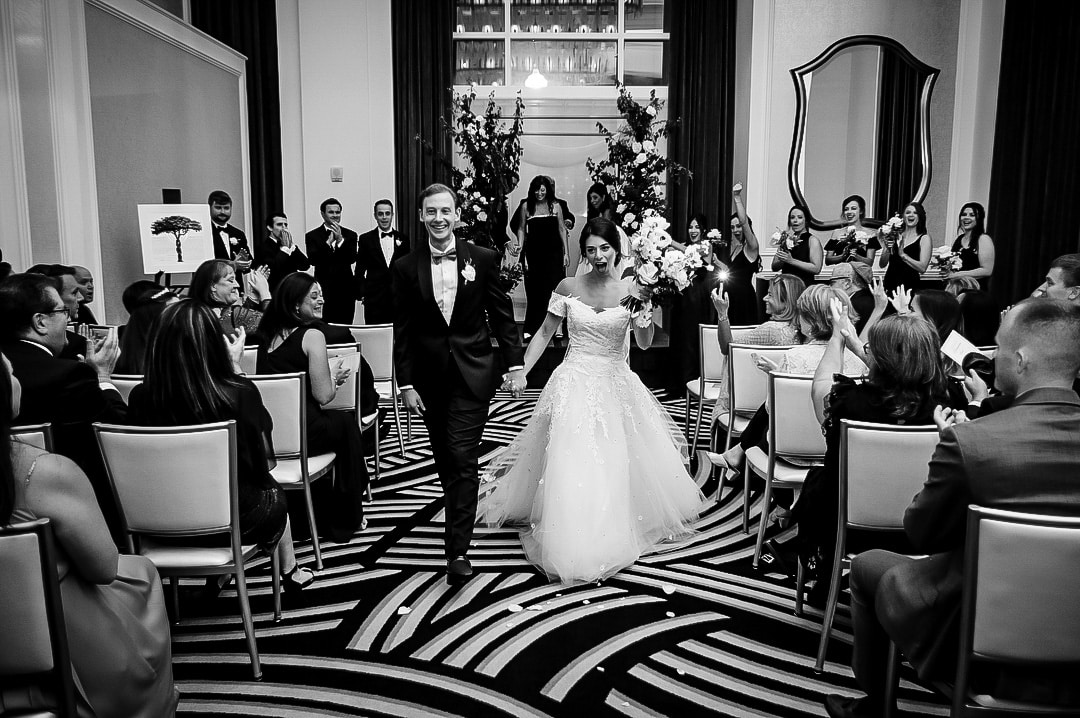 A bride and groom celebrate as they walk down the aisle after their elegant wedding at the Hotel Monaco in Pittsburgh.