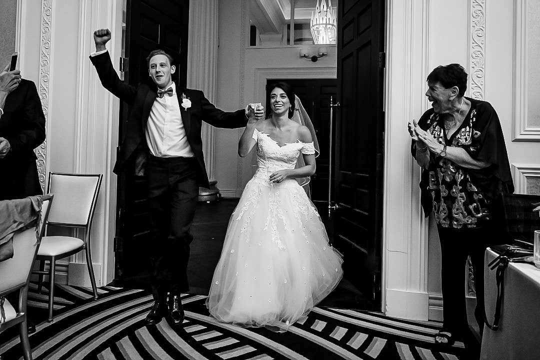 A groom raises his hand in celebration as he and the bride enter the ballroom during their wedding at the Hotel Monaco in Pittsburgh.