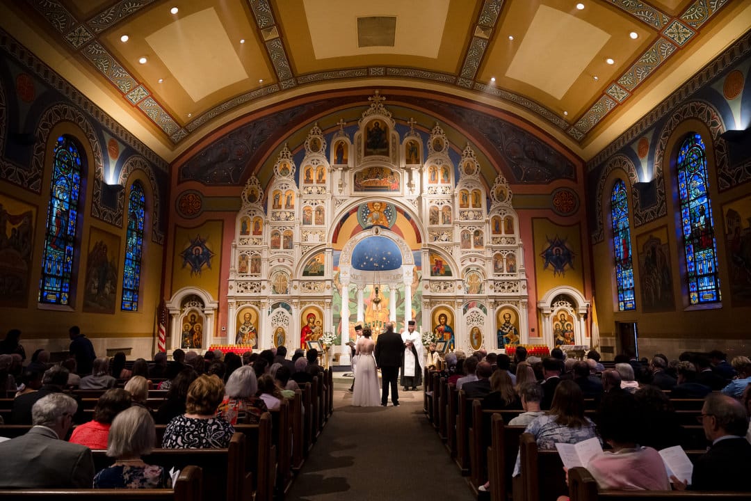 The screen decorated with icons is at the center of the image while a bride and groom stand together during their wedding ceremony at Saint John Chrysostom church in Pittsburgh.