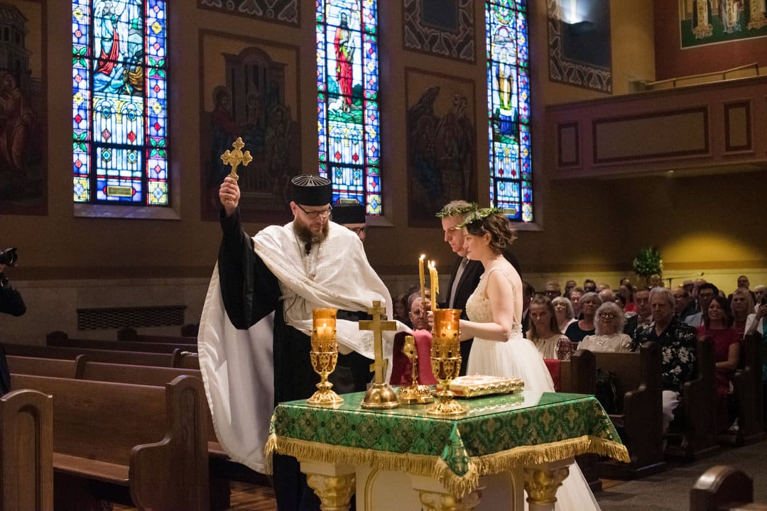 A priest holding up a crucifix leads a couple as they circle a table in Saint John Chrysostom church during their wedding.