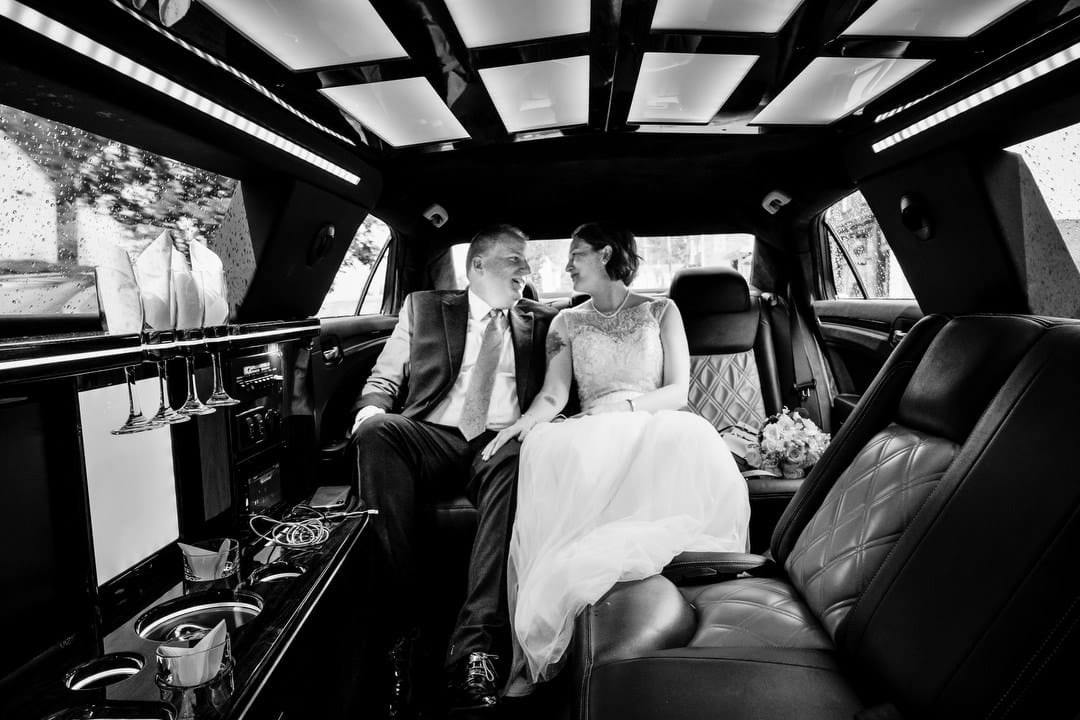 A bride and groom sit together at the back of a stretch limousine after their wedding.