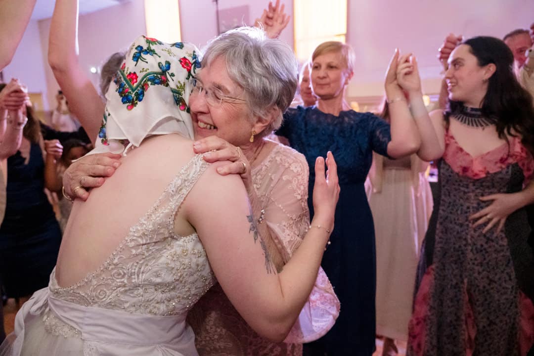 A bride wearing a babushka is embraced by her mother as guests surround them on the dance floor at her Saint Nicholas Cathedral Room wedding.