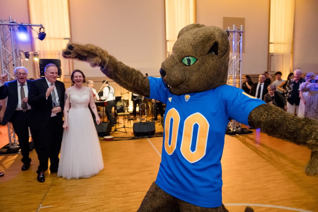 Roc the Pittsburgh Panthers mascot dances with his arms out while a bride and groom watch during their Saint Nicholas Cathedral Room wedding.