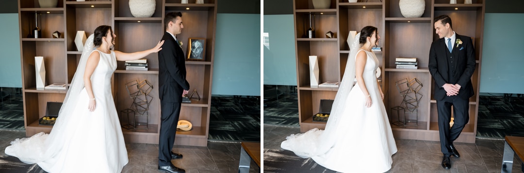 In The Art Room Wedding, a bride in a white gown gently taps the groom on the shoulder. They turn to each other with glowing smiles, standing before a wooden bookshelf in a modern space with dark flooring.