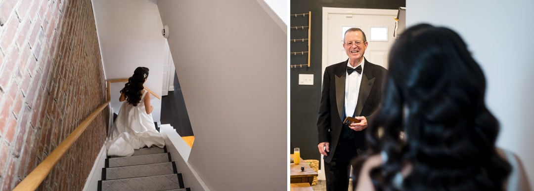 A bride in a white dress walks down the stairs on the left; on the right, an older man in a tuxedo smiles warmly at her inside a home, seen from behind the bride’s head.