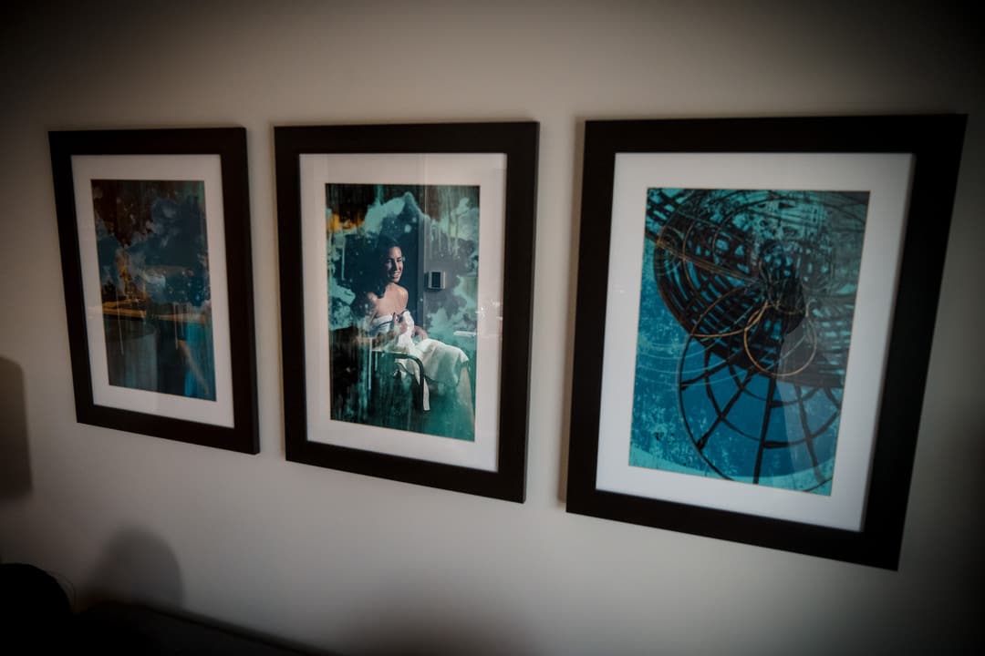 Three framed abstract artworks hang on a white wall. The left and right images feature blue and green tones, while the center image depicts a person holding a white dog, also overlaid with blue-green textures.