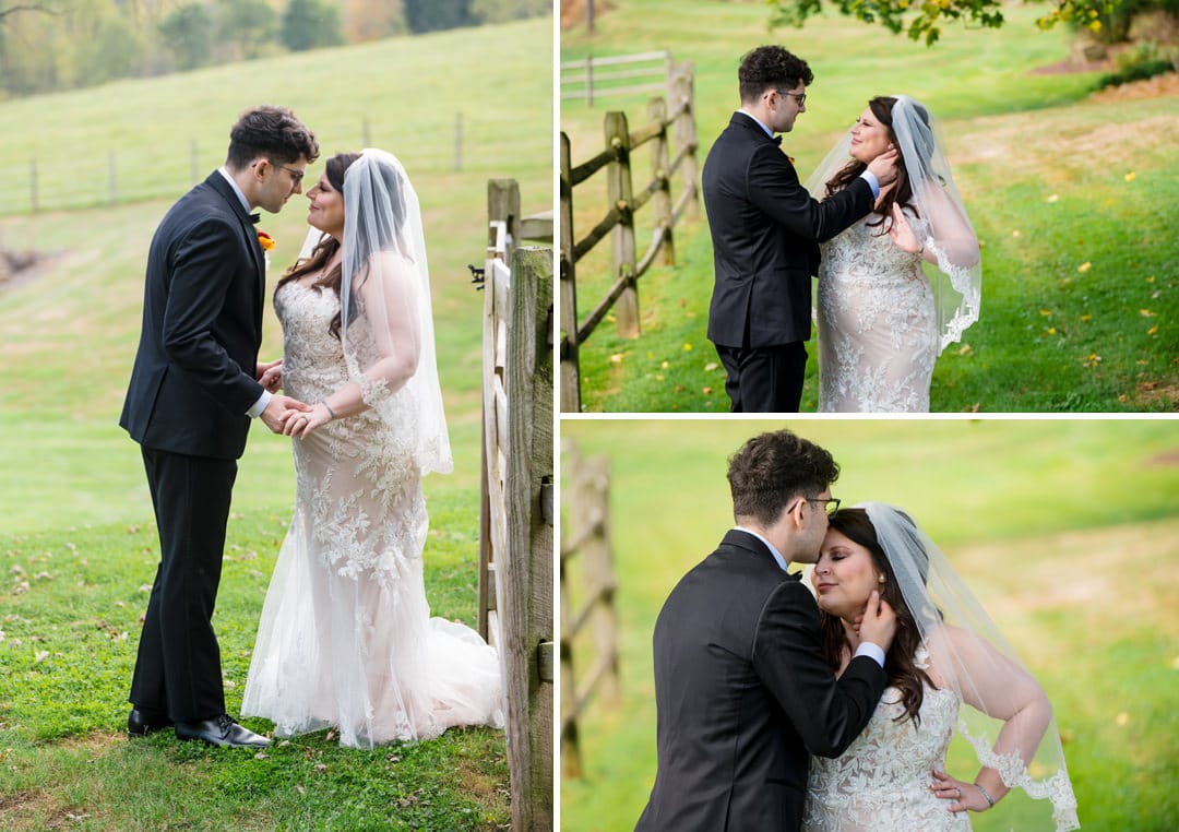 A bride and groom stand together by a wooden fence in a grassy field, holding hands and sharing intimate, loving moments on their wedding day. The bride wears a lace dress and veil; the groom is in a black suit.